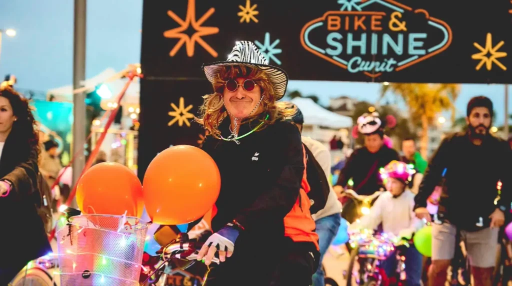 Participant disfressat amb bicicleta i globus sota l'arc de sortida del Bike & Shine Cunit