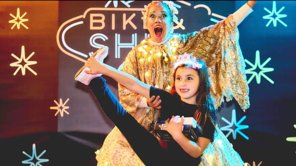 Nena ballant amb la Miss Shine davant el rètol de neó del Bike & Shine